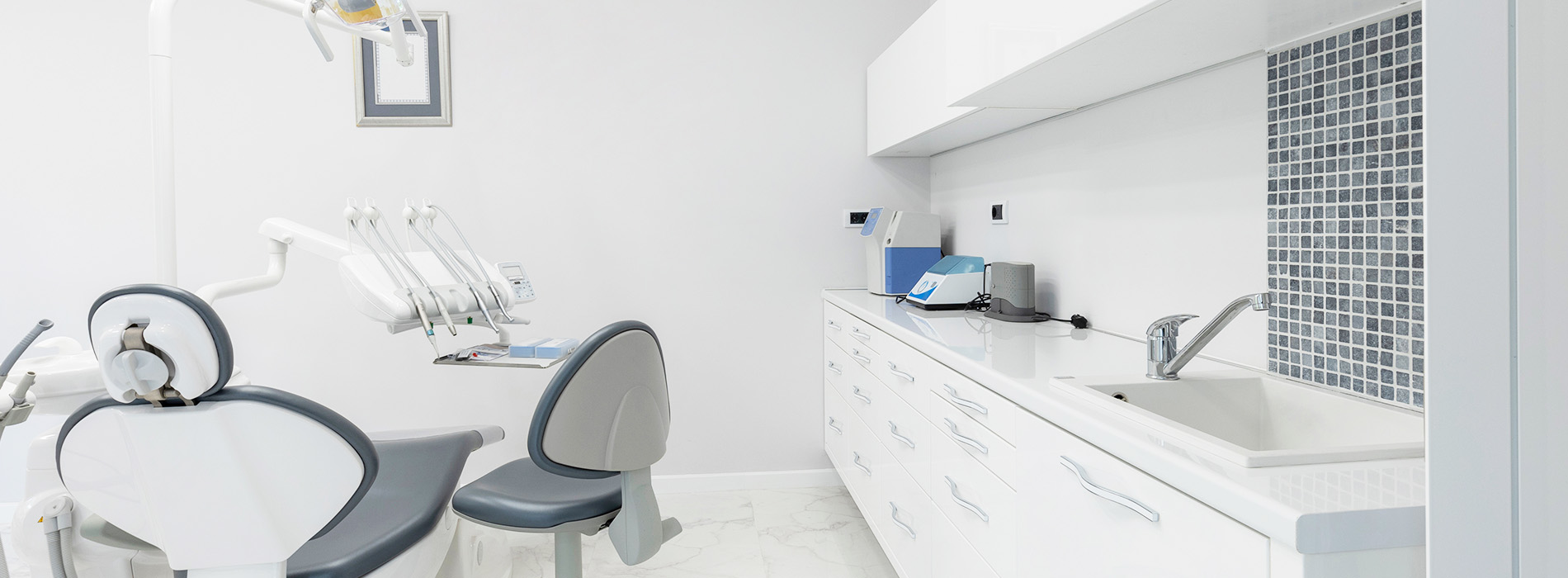 The image shows a modern dental clinic interior with various pieces of equipment, including a dental chair and an X-ray machine.